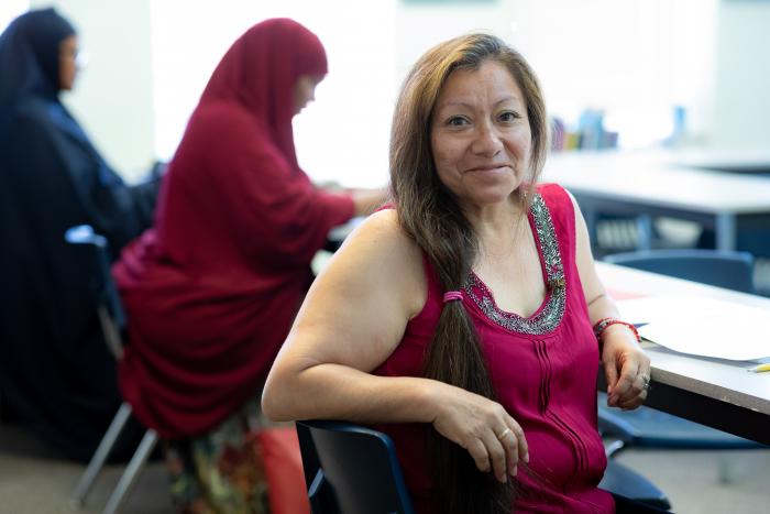 Student sits in classroom and smiles into the camera