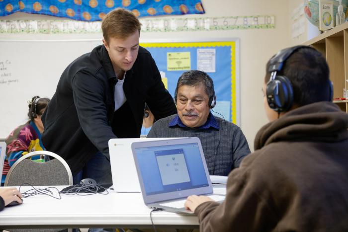 Volunteer helps students working on computers in classroom.