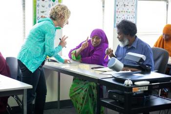 Adult ESL teacher talking to two learners sitting at a table