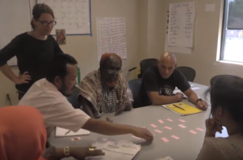 Adult ESL learners playing a game while the teacher looks on