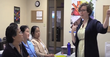 Adult ESL teacher talking to three learners sitting at a table