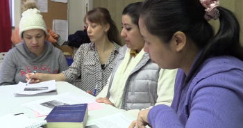 Adult ESL teacher helping three learners with a reading activity