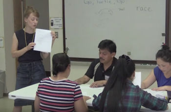 Adult ESL teacher talking to two learners sitting at a table