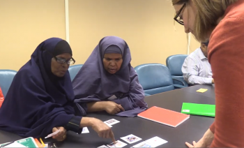 Adult ESL teacher talking to two learners sitting at a table