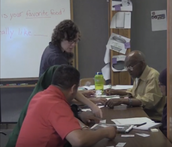 Adult ESL teacher talking to two learners sitting at a table