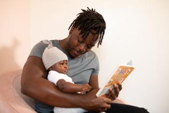 Smiling Black father reading a book to his small baby