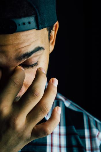 Young man in a backwards baseball cap pinching the bridge of his nose