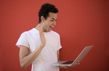Smiling man holding a computer and waving