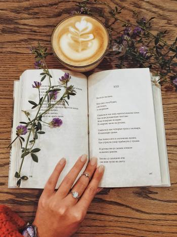 hand holding open a book of poetry with flowers and a cup of coffee 