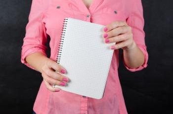 person in a pink shirt holding a blank notebook in front of them