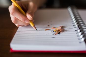 hand holding a pencil over a notebook with pencil shavings on the page