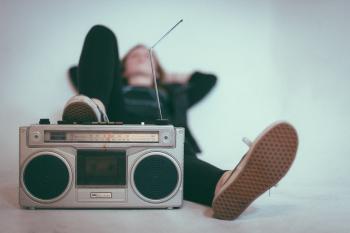 person lying on the floor with their hands behind their head and their foot propped up on a portable radio