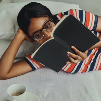 black woman reclining and reading a novel with a cup of tea