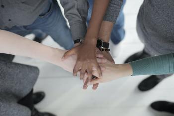 People huddled up in a circle, resting their hands on top of each other at the center