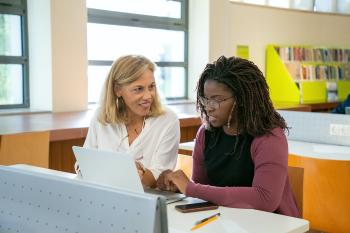 a white teacher sits and talks with a black adult student