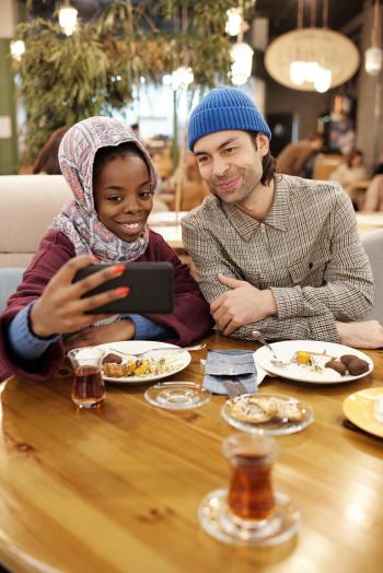 a Muslim woman takes a selfie with a man with a meal and tea in the foreground 