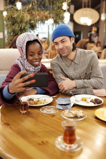 a Muslim woman takes a selfie with a man with a meal and tea in the foreground