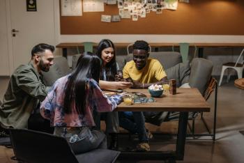 four adults of various races sit around a table playing a card game