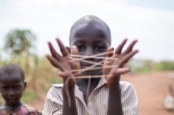 Ugandan boy holding a string woven between his fingers in front of his face