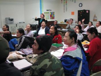 A class of beginning level adult ESL students read together off of the board