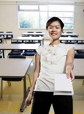 woman in classroom holding out a notebook