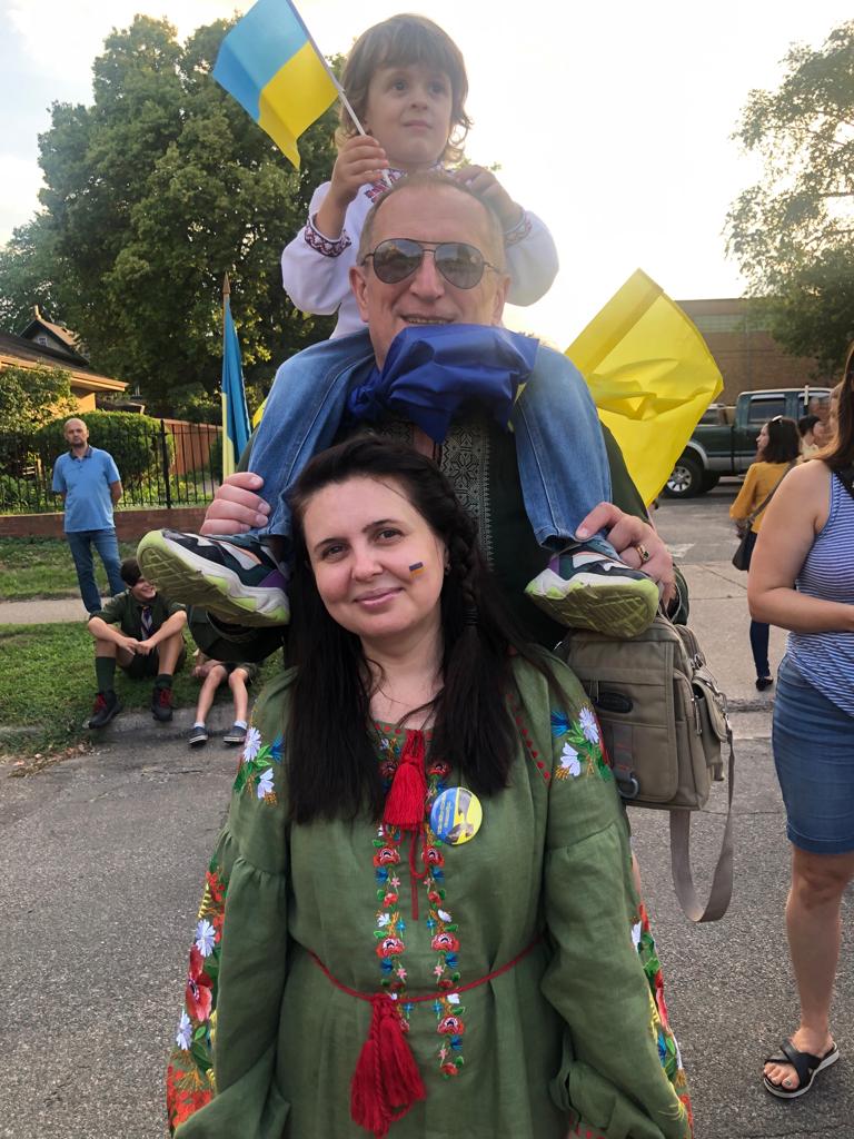 Photo shows Yuliia, Sergei and Ivan standing together as a family, waving Ukrainian flags.