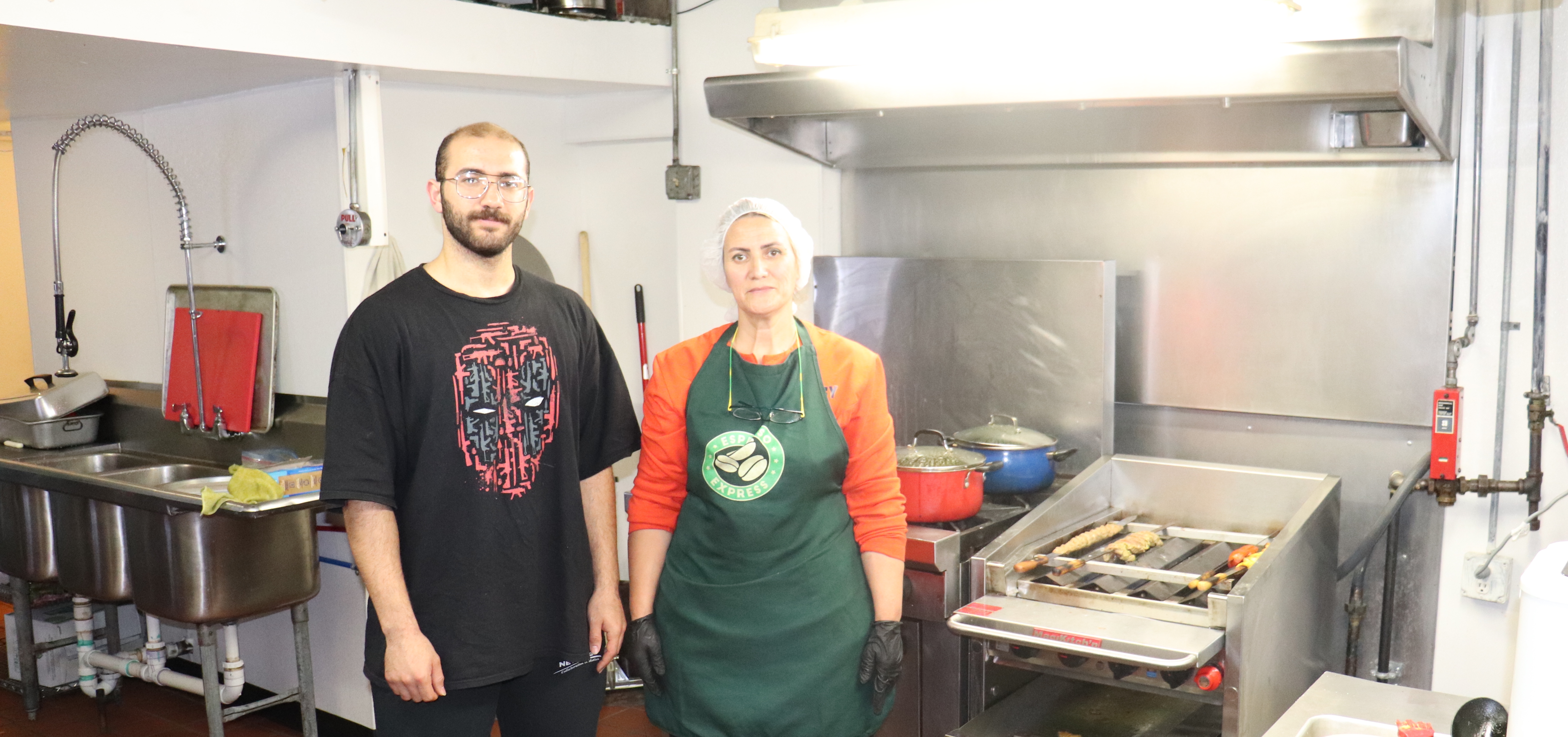 Amir and his mother stand in front of the kebab grill in Nader restaurant
