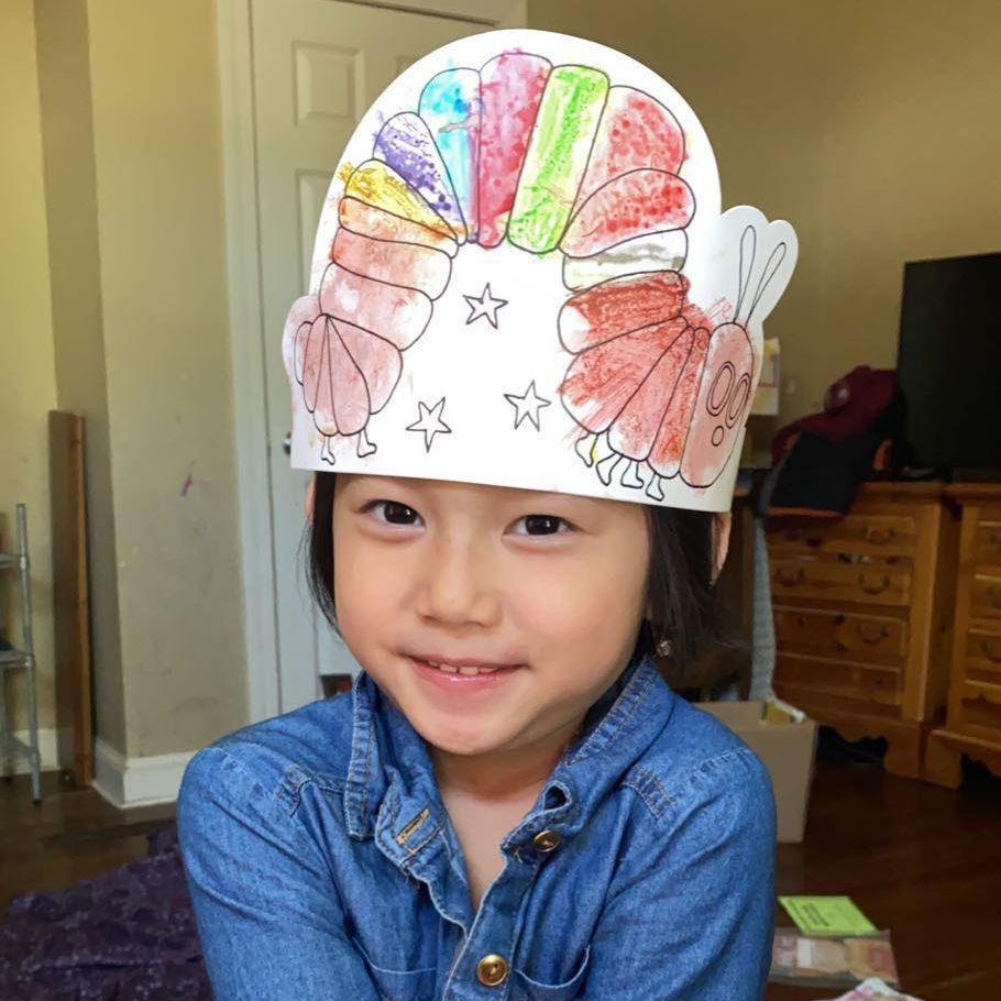 Preschool student is smiling wearing a hat they made as a craft.